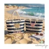 bolsos de playa de rayas marineras azules y blancas sobre la arena con el mar de fondo. El bolso izquierdo tiene el texto "Nuestra PROFE Marisa tiene mucha CLASE" y el derecho tiene nombres de alumnos alrededor de un corazón rosa con la frase "TE QUEREMOS".