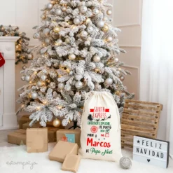 Saco Navidad personalizado Santa Express con nombre Marcos, diseño de Papá Noel, 100 % algodón ecológico, frente a árbol nevado con regalos.