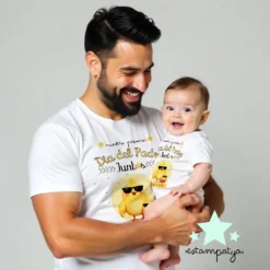 "Papá y su bebé sonriente visten camisetas blancas con diseño de pollito y la frase 'Nuestro primer Día del Padre juntos'."