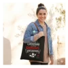 Bolsa de tela negra para profesora con frase divertida sobre corregir examenes y asas marrones, modelo la lleva puesta