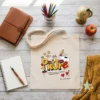 Bolsa de tela personalizada para regalo de profesora con diseño de lápices y nombre de alumno sobre mesa decorada.